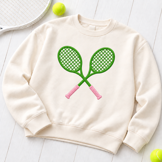 Cross Court ivory embroidered sweatshirt flat lay with straight crossed green tennis rackets and pink handles